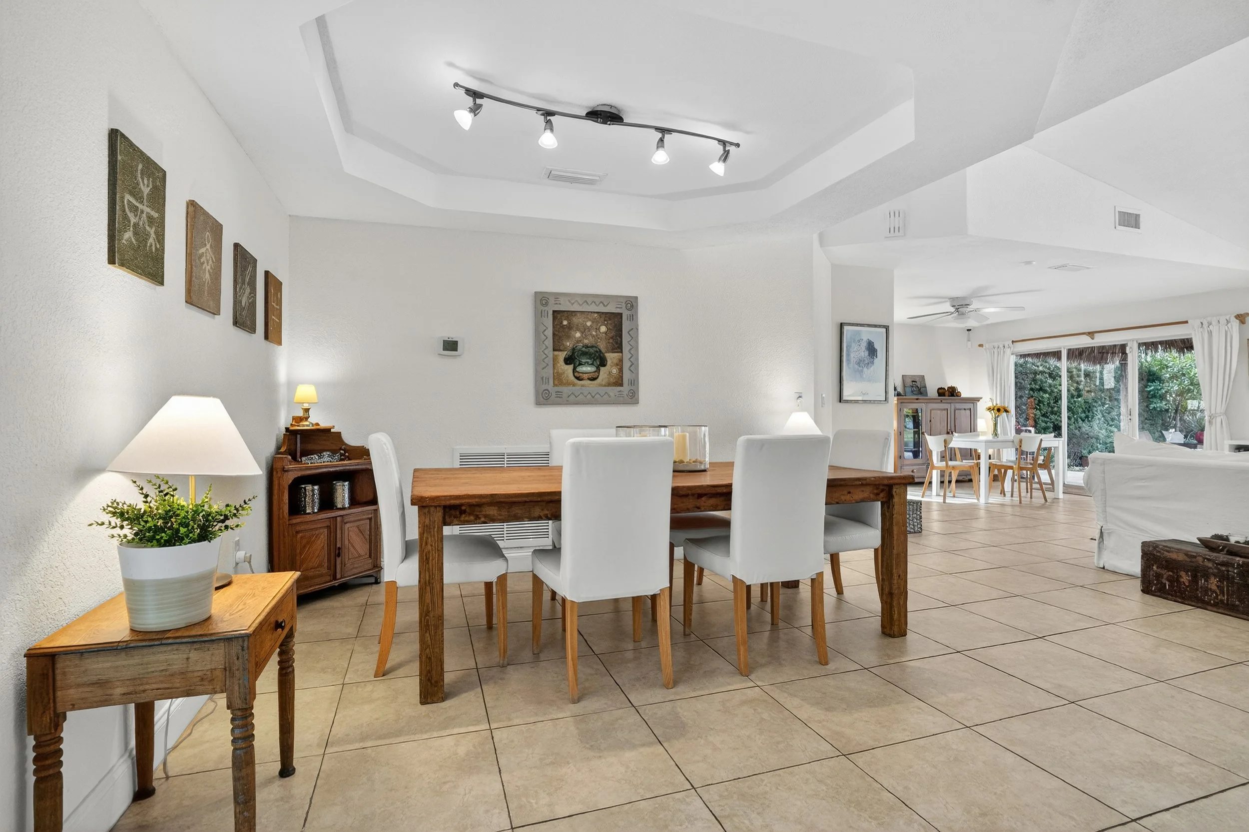 Spacious dining room featuring a wooden table and upholstered chairs within an open-concept living space. Natural light flows through large windows, highlighting neutral tones, framed artwork, and cozy modern decor.
