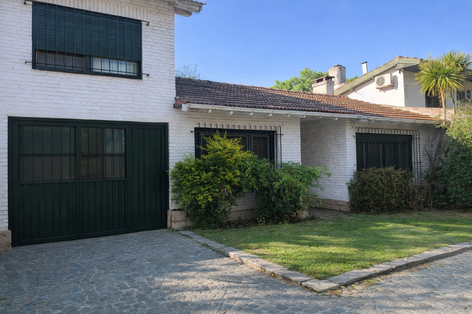 Front exterior view of a detached family home in San Isidro, featuring a white brick facade, green lawn, and driveway in a quiet residential setting.