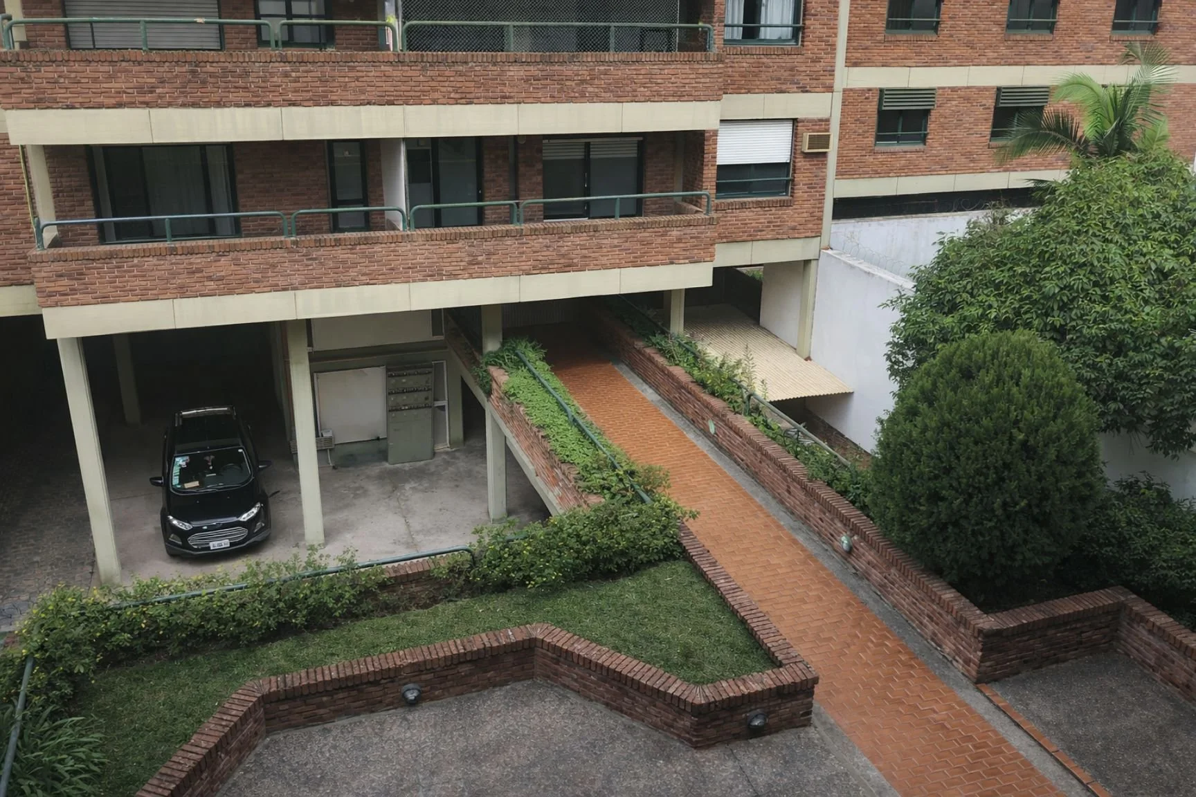 Common outdoor areas of a residential apartment building in San Isidro, featuring brick walkways, green spaces, and garage access