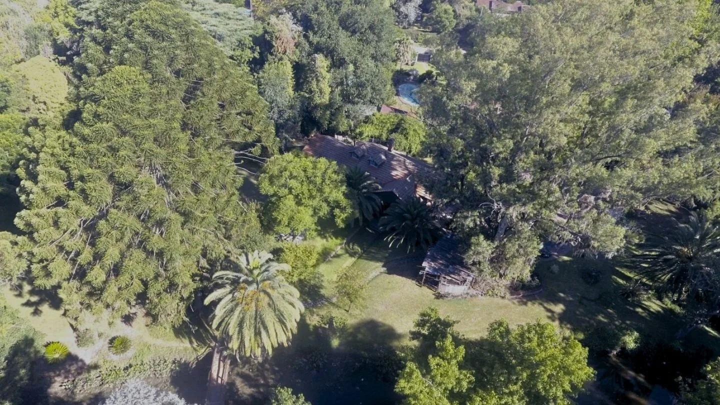 Aerial view of a private brick home surrounded by mature trees and lush gardens in Ingeniero Maschwitz, Argentina.