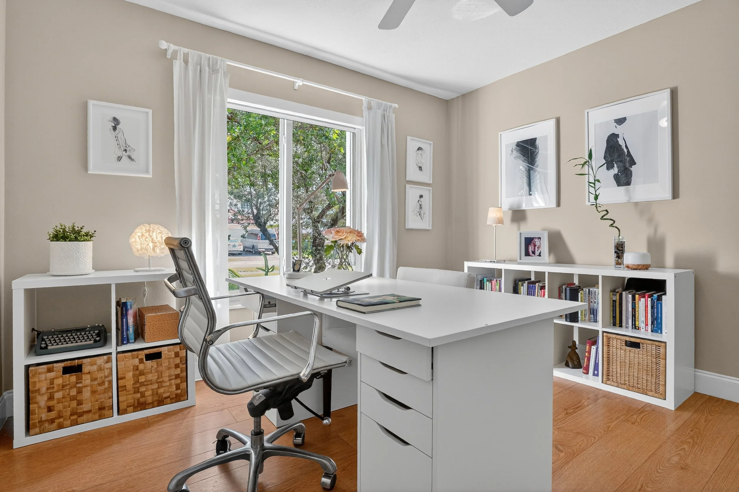 Bright home office with white desk, ergonomic chair, built-in shelving, and large window bringing in natural light and garden views. Neutral tones and minimalist design create a calm, organized workspace.