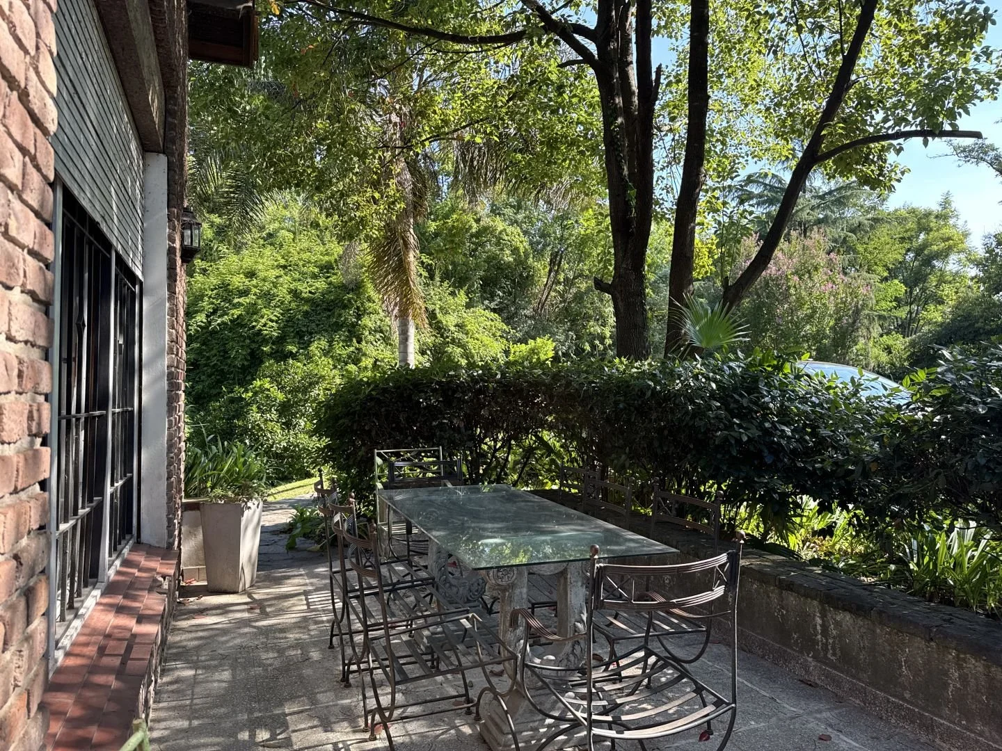 Private garden dining area with outdoor table surrounded by mature trees and lush greenery.