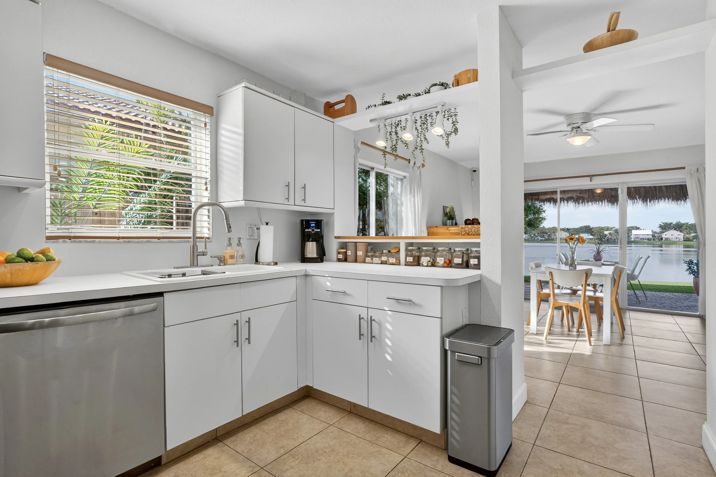 Bright white kitchen with modern cabinetry, stainless steel appliances, and natural light. Corner layout opens to a dining area and sliding glass doors with lake views, blending functionality with serene indoor outdoor living.
