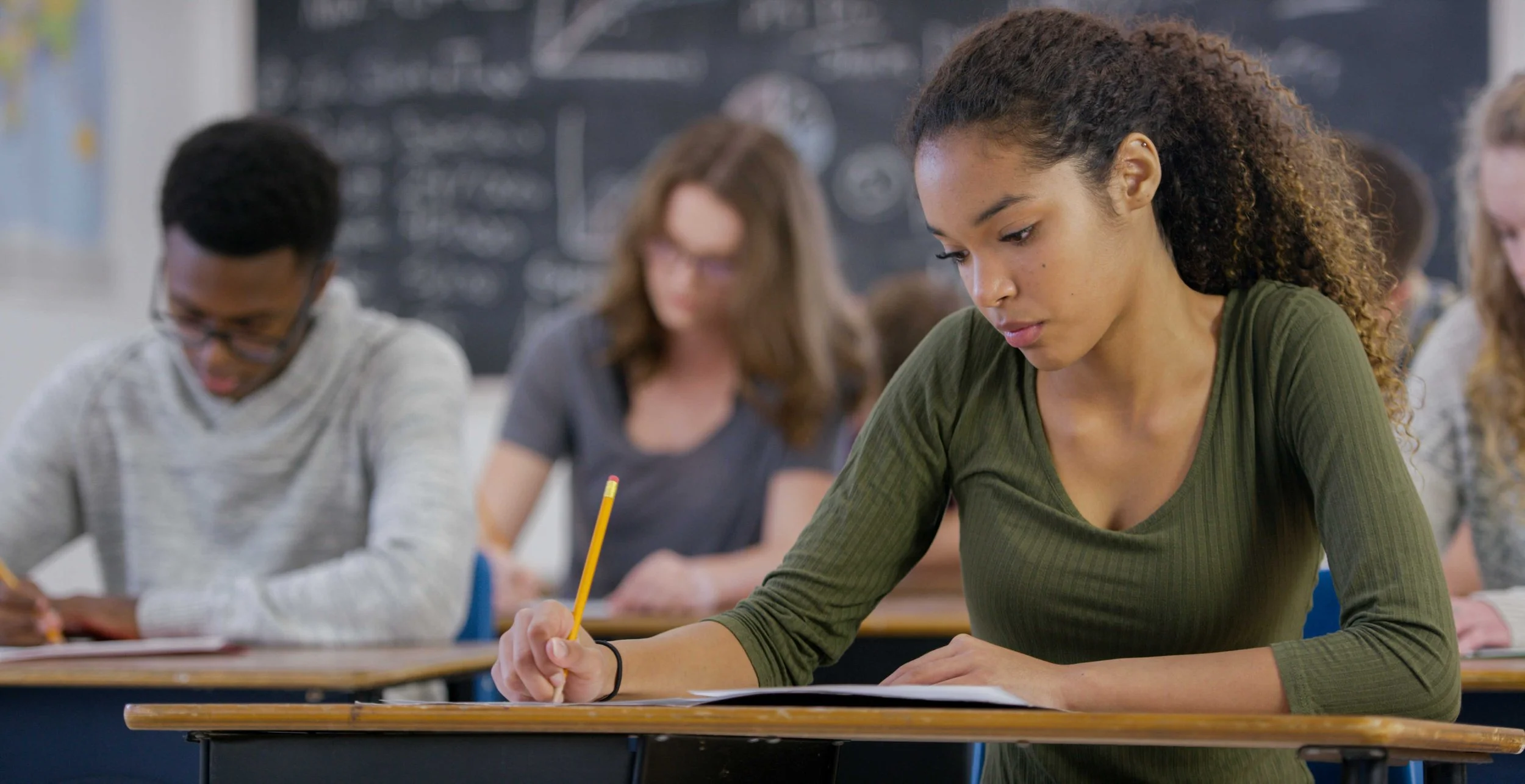 High school students sit at their desks, working on papers, in a classroom.