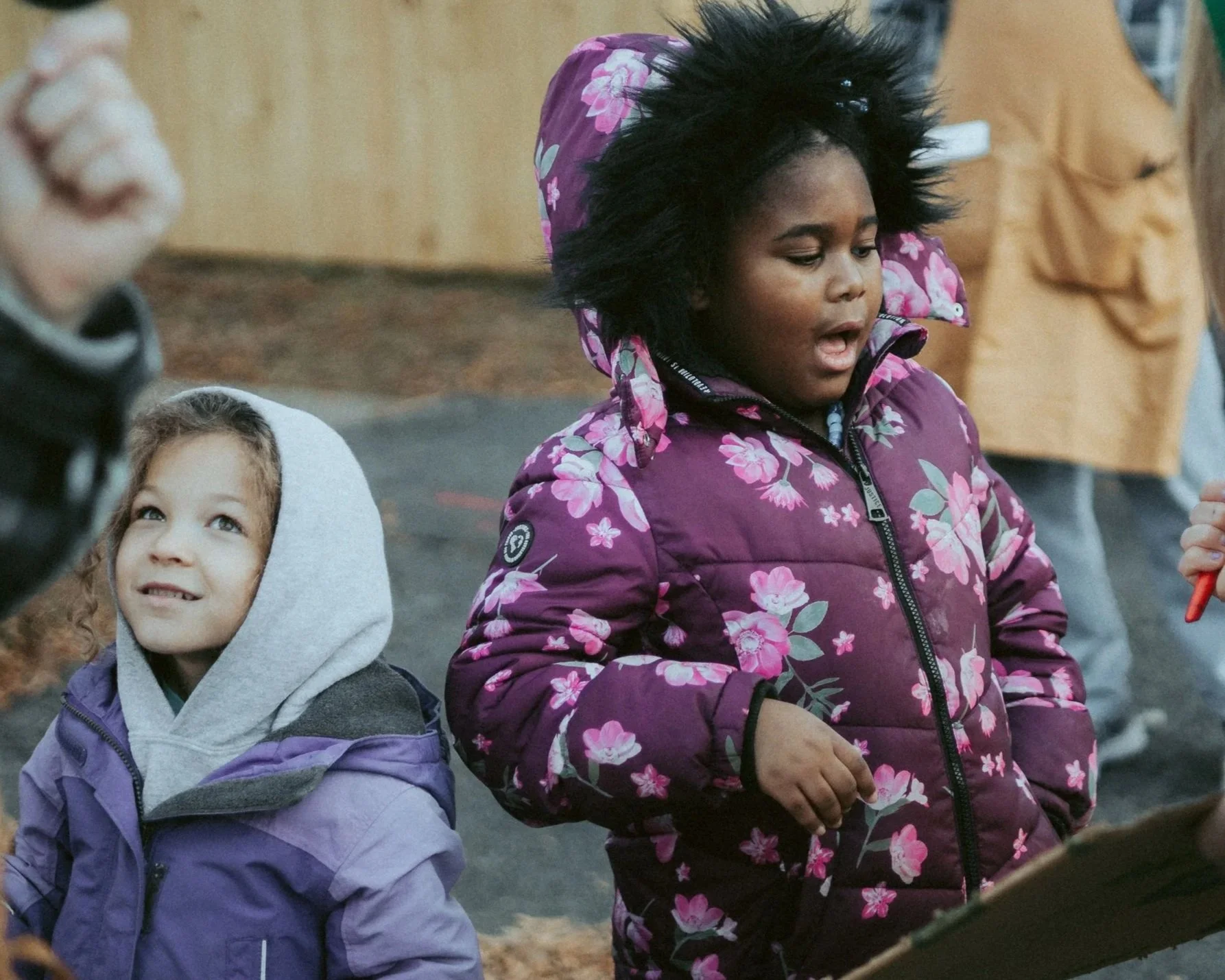 Two young girls stand together outside, in winter coats.