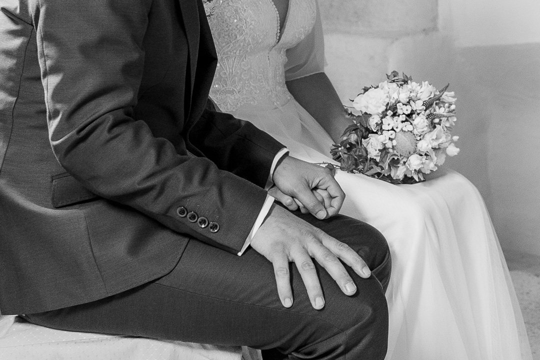 Brautpaar in Hochzeitskleidung, sitzt nebeneinander, Braut hält Blumenstrauß, Schwarz-Weiß-Foto.