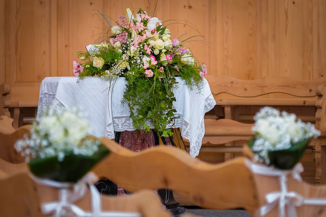 Blumengesteck auf einem Tisch mit weißer Tischdecke in einer Holzkapelle.