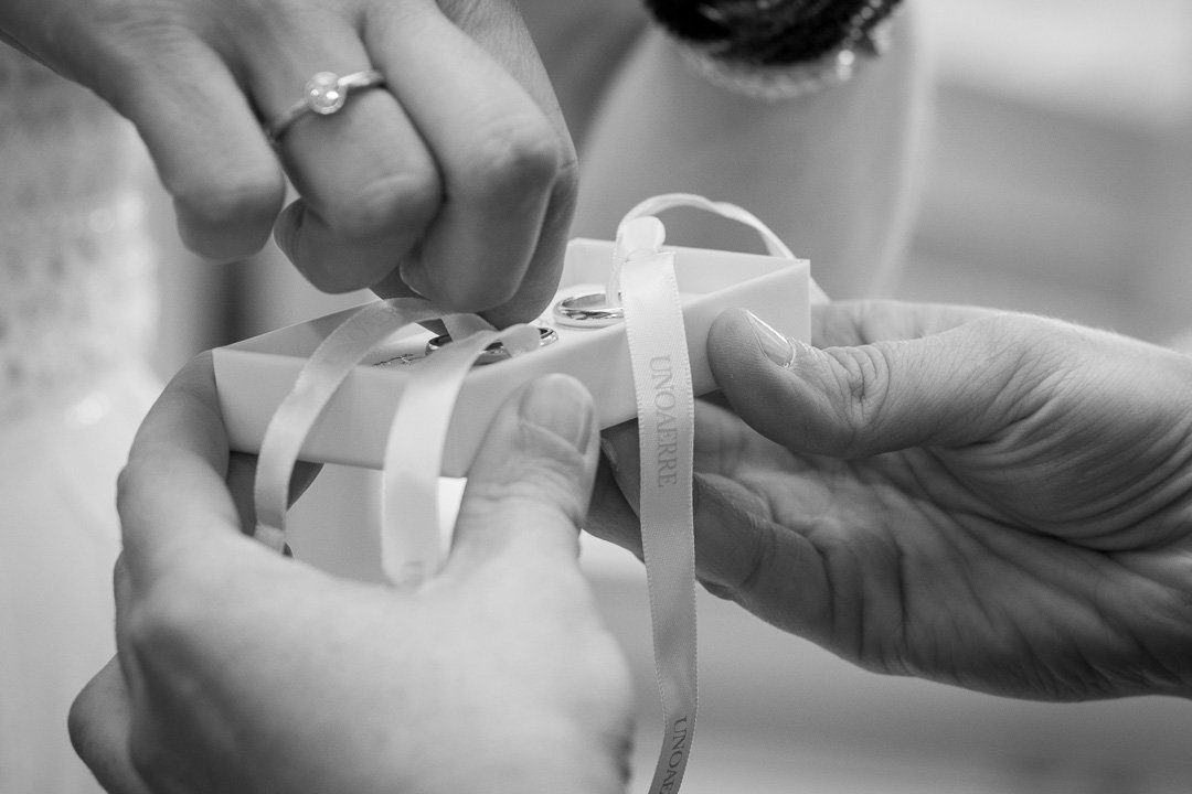 Zwei Hände öffnen eine Geschenkbox mit einem Ring darin. Ein Band ist um die Box gewickelt, und eine Person trägt einen Verlobungsring.