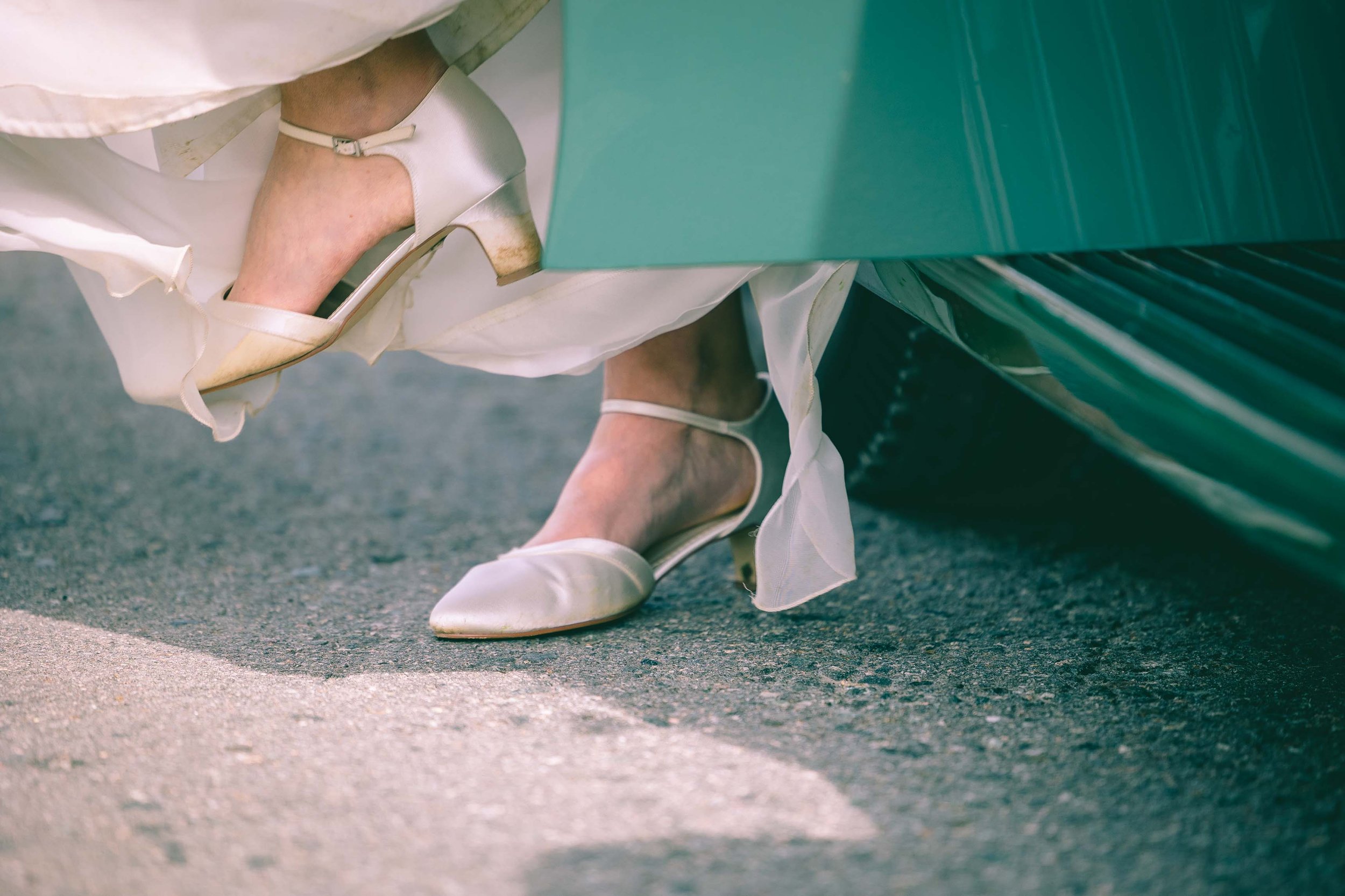 Nahaufnahme von einer Person in eleganten, weißen Schuhen, die aus einem Auto steigt.