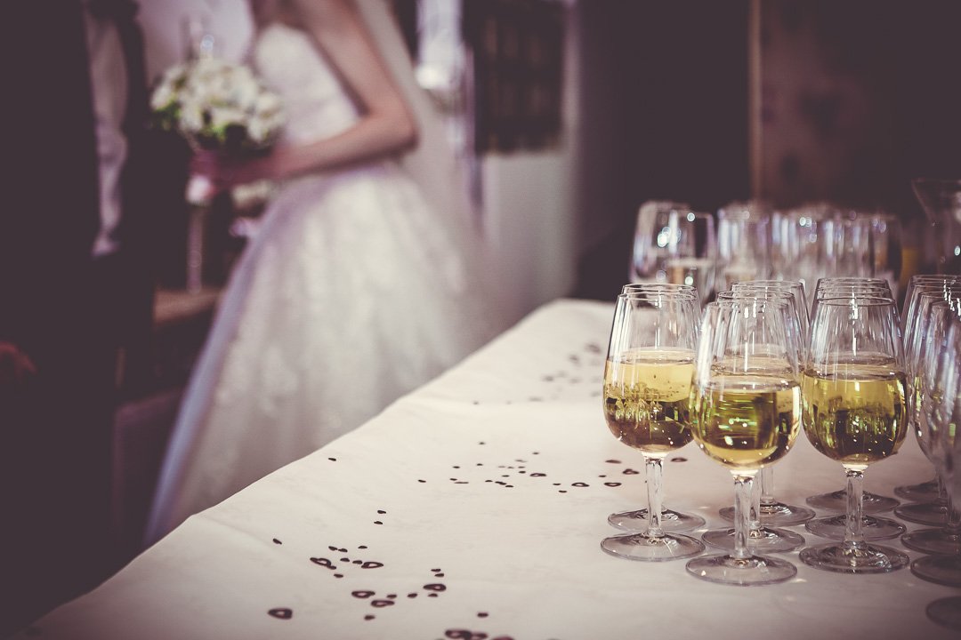 Hochzeitsszene mit einer Braut im Hintergrund und gefüllten Sektgläsern im Vordergrund auf einem dekorierten Tisch.