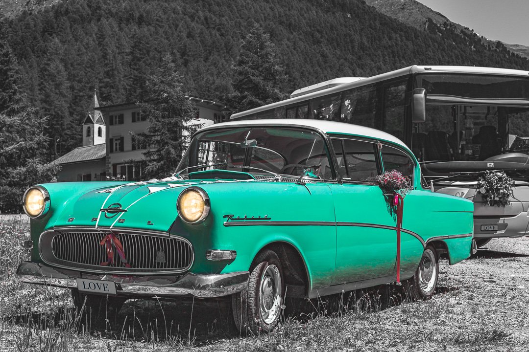Grünes Oldtimer-Auto mit Deko, Kirche im Hintergrund, Schwarz-Weiß-Landschaft.