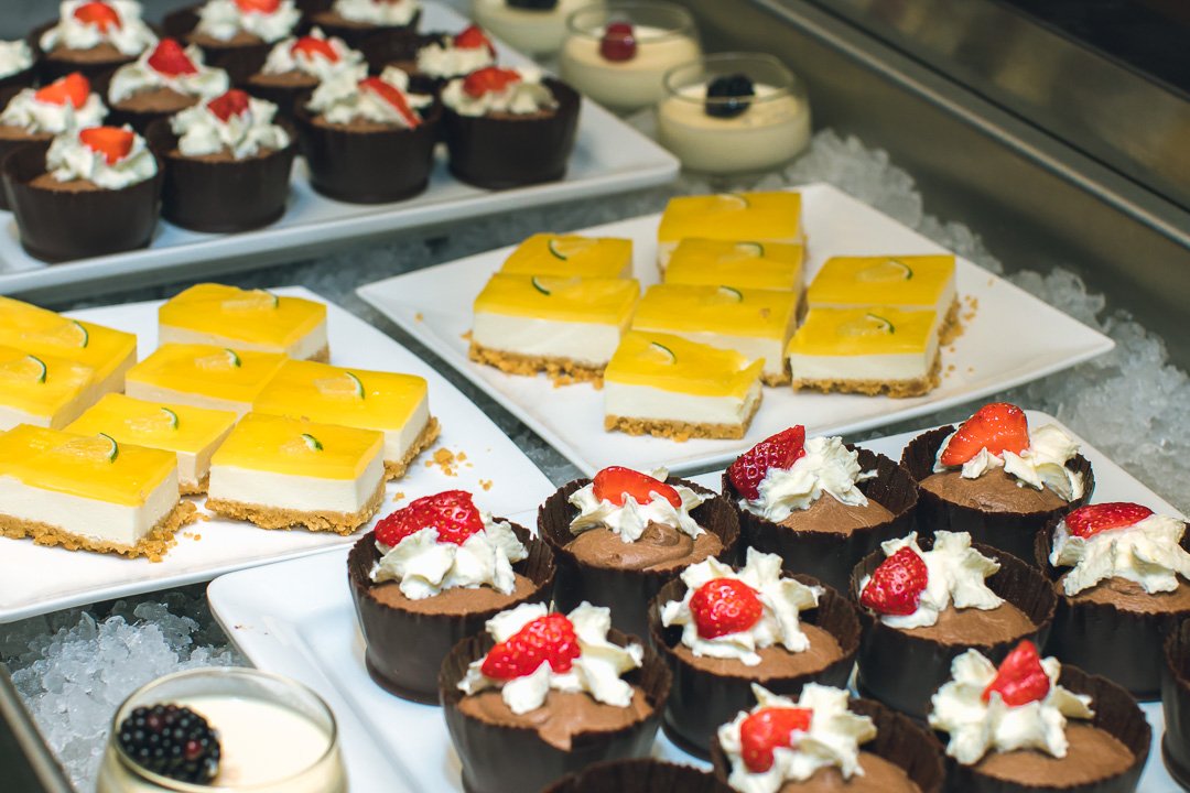 Verschiedene Desserts auf Tellern, darunter Schokoladenmousse mit Sahne und Erdbeeren, Zitronen-Törtchen und Dessertgläser mit Beeren.