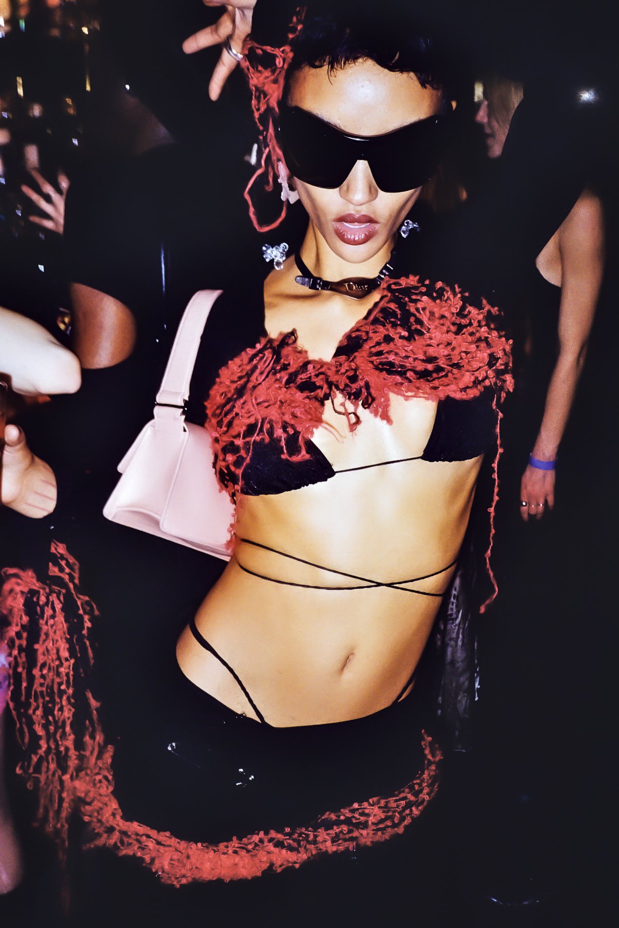 Une femme portant des vêtements colorés et accessoires de mode à une fête ou un spectacle, portant des lunettes de soleil noires et un collier noir.