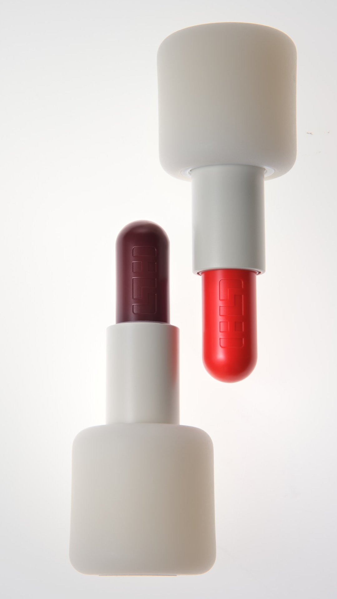Deux capsules de médicaments de couleurs différentes, rouge et violette, posées sur des supports blancs, avec un fond blanc lumineux.