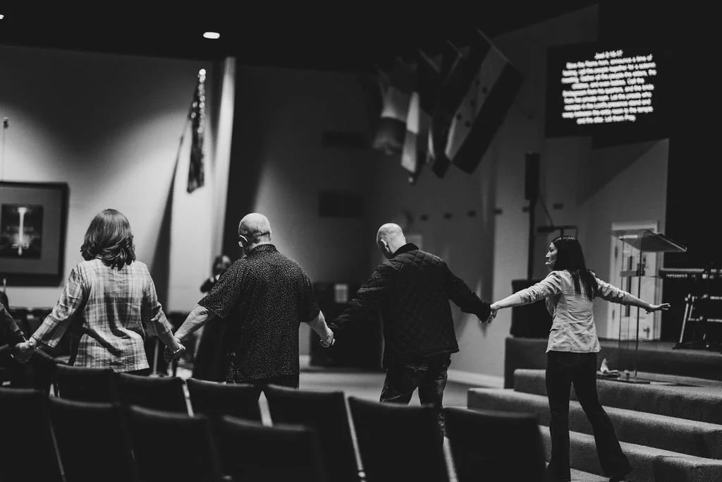 Group of people holding hands in a circle inside a church or auditorium.