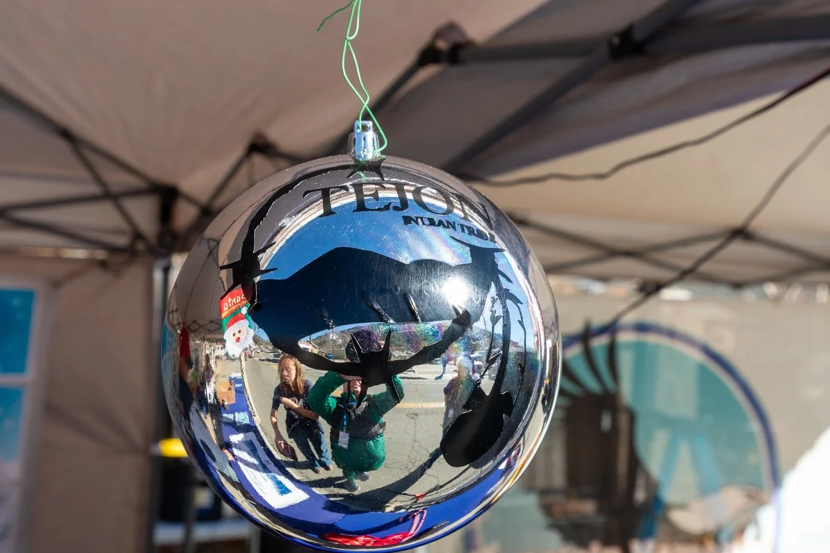 A shiny spherical Christmas ornament reflecting the outdoor scene, including people and tents.
