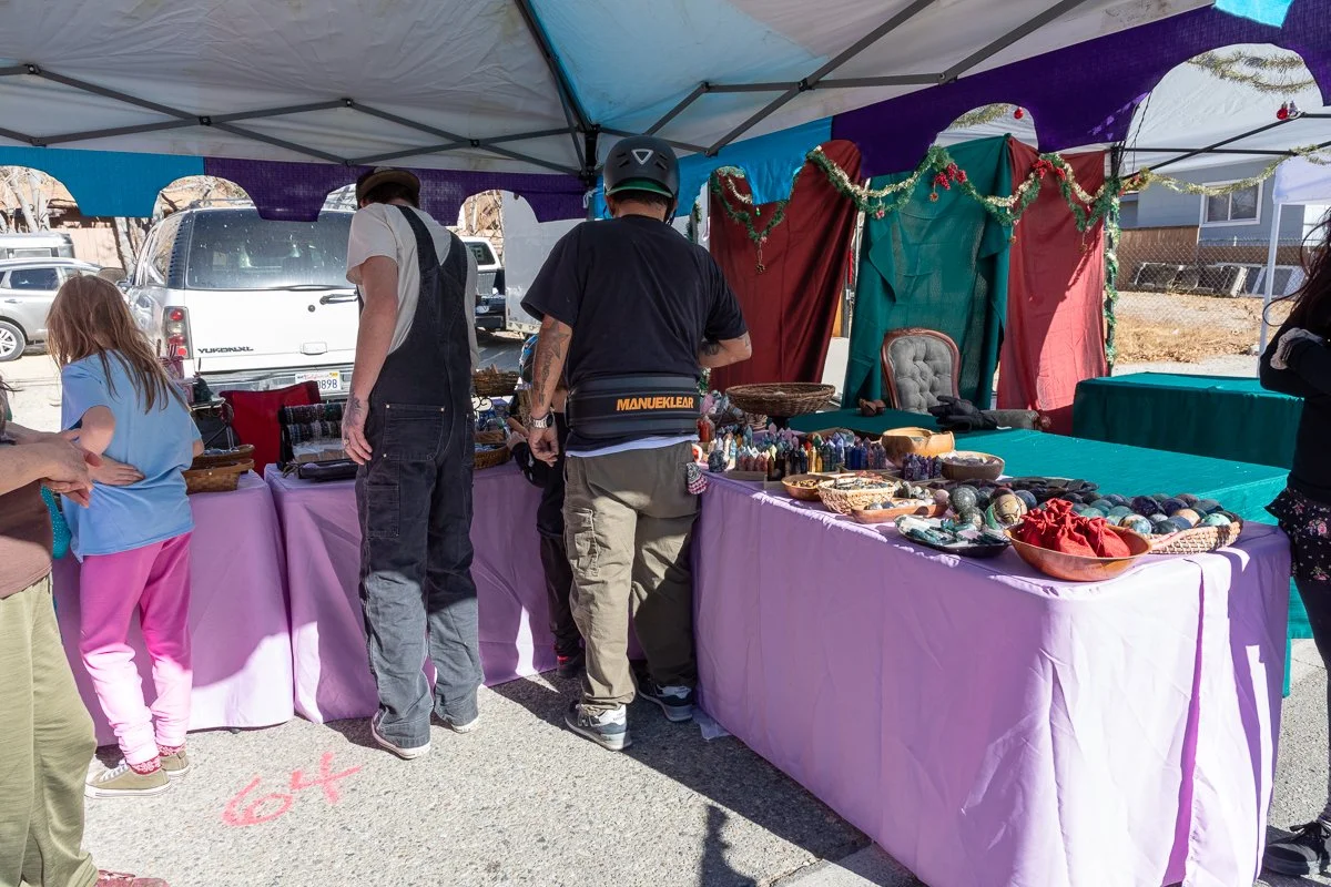 People browsing at an outdoor craft fair under a tent, with tables displaying various jewelry and decorative items.