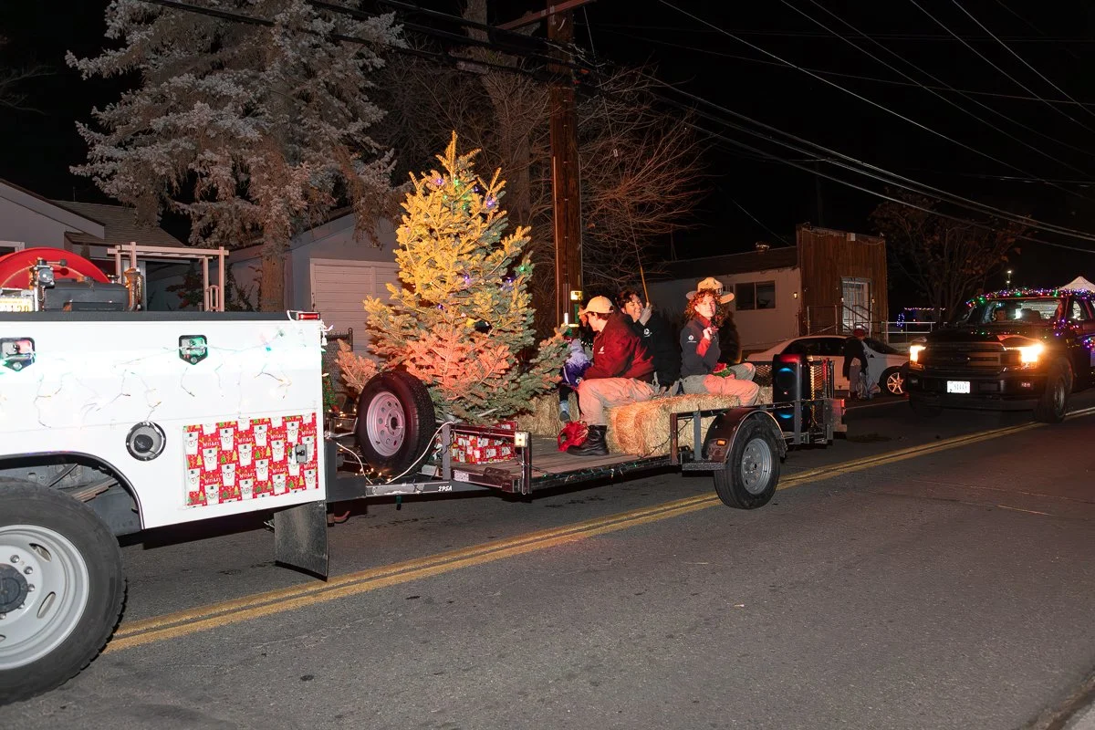 People sitting on a decorated float with a Christmas tree, participating in a nighttime holiday parade.