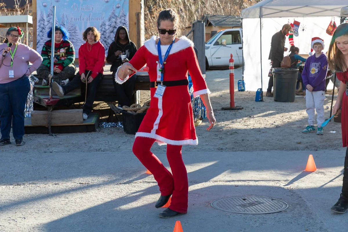 Woman dressed as Santa Claus dancing outdoors at a Christmas event with children and adults watching.