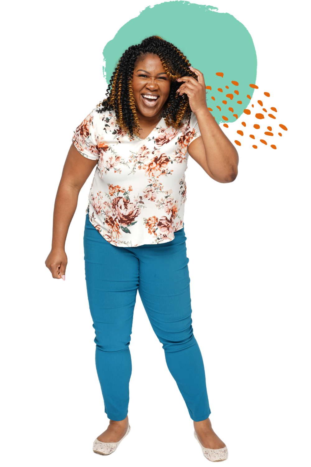 A joyful woman with curly hair and a floral blouse laughing, standing with one hand touching her head and wearing blue pants and flats.