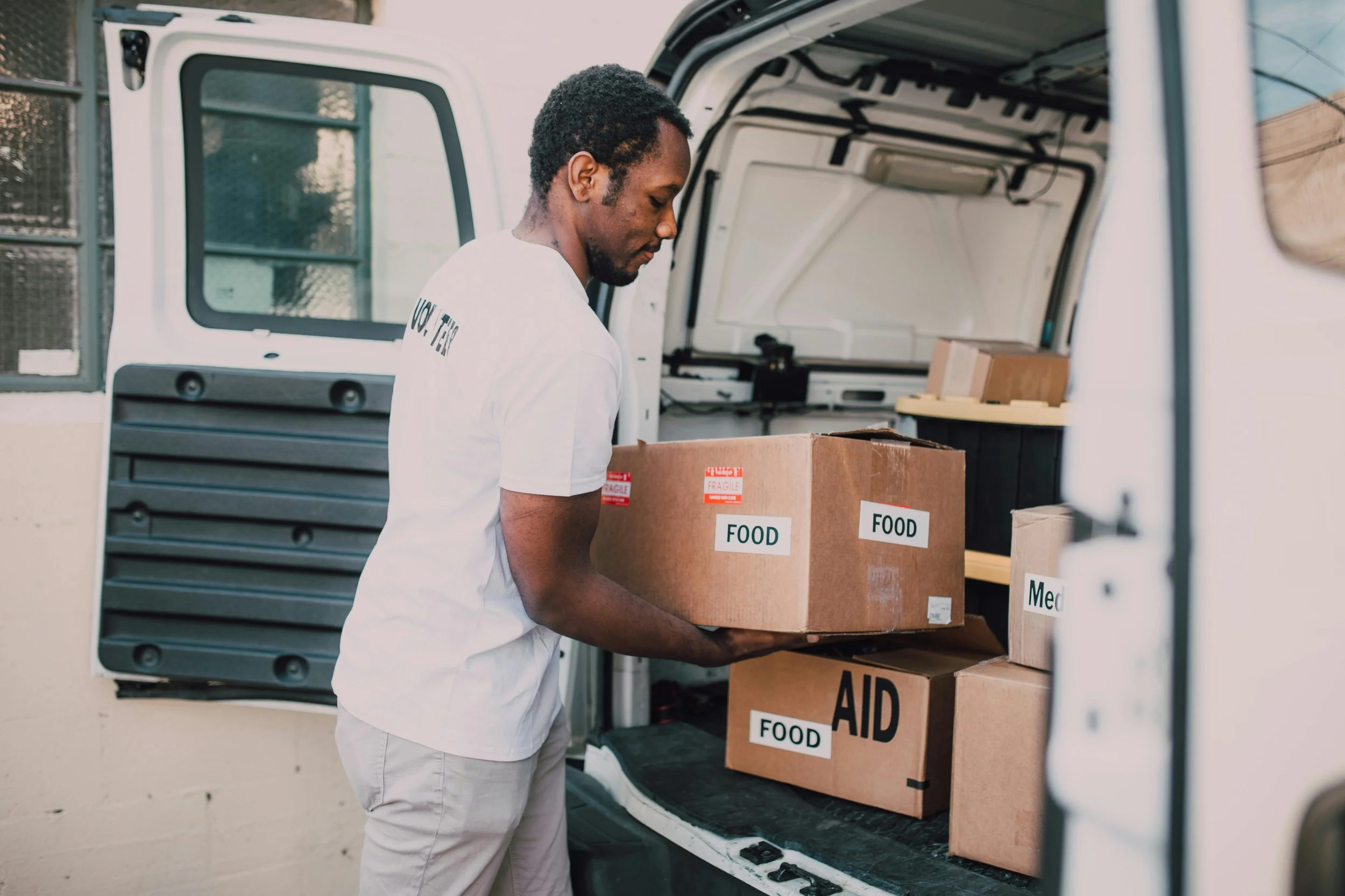 A man loading boxes labeled 'FOOD' and 'AID' into the back of a white delivery van.