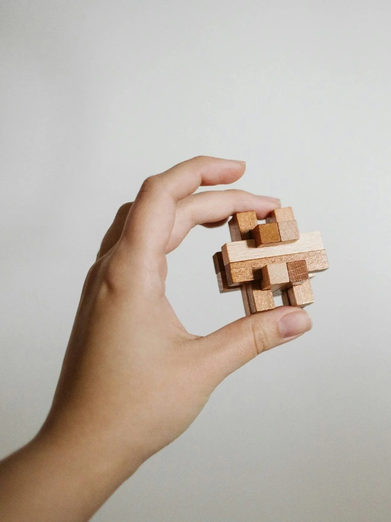 A person holding a small wooden geometric puzzle with a plain, light-colored wall background.