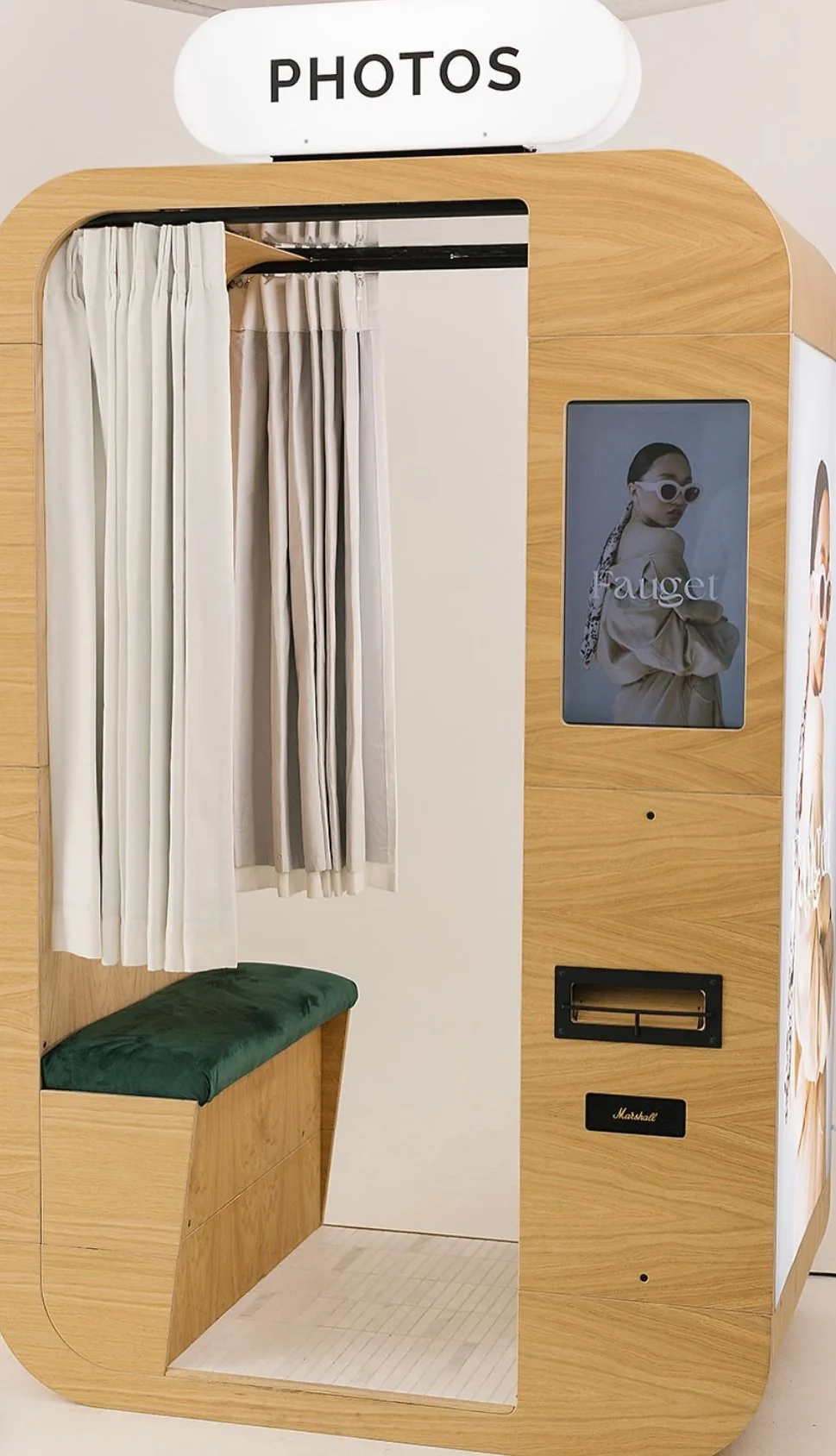 Photo booth with curtains, a green bench, a poster of a woman with sunglasses, and a sign labeled 'PHOTOS' on top.