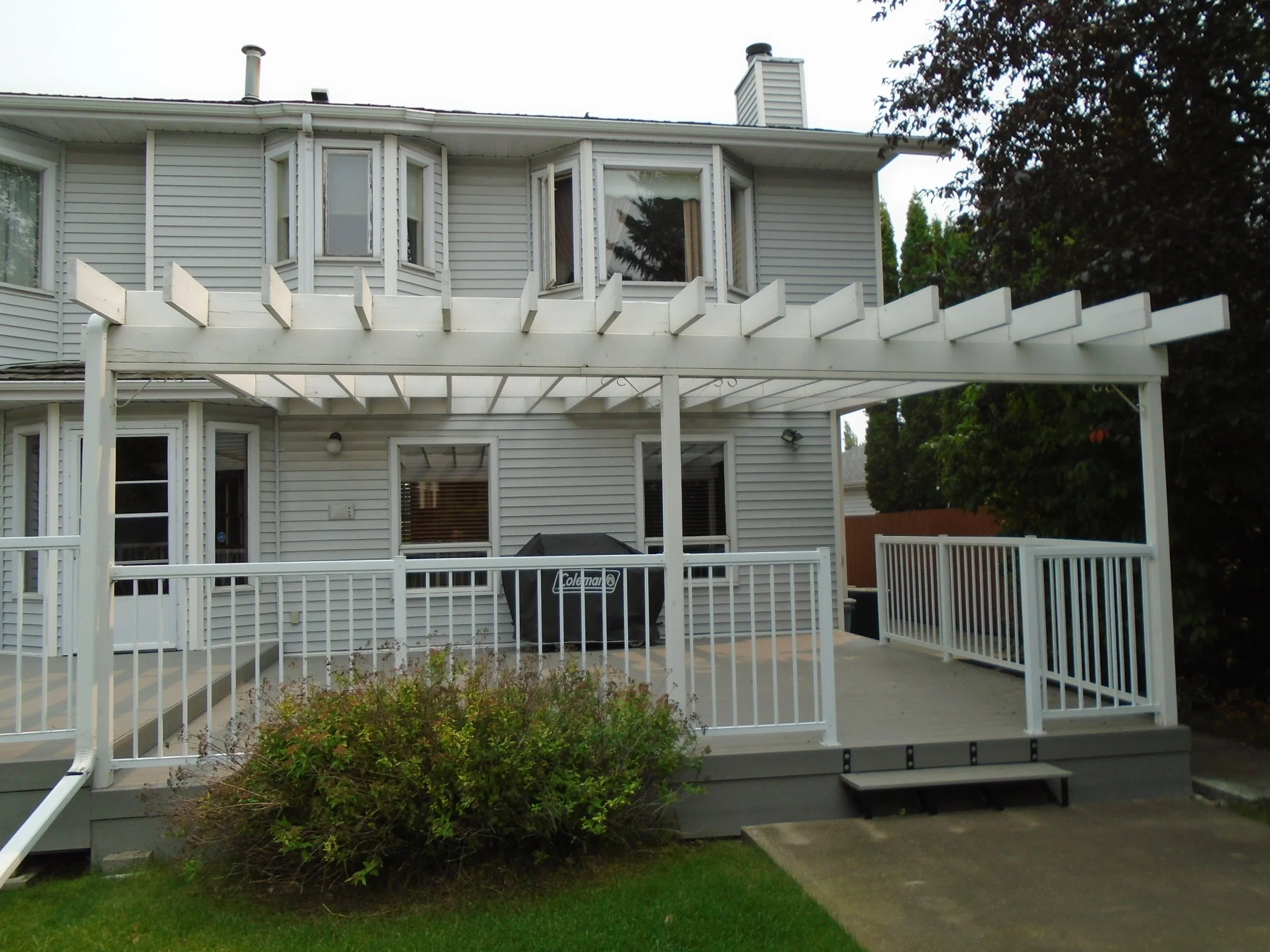 Rear patio with over sized pergola attached to house exterior wall. 