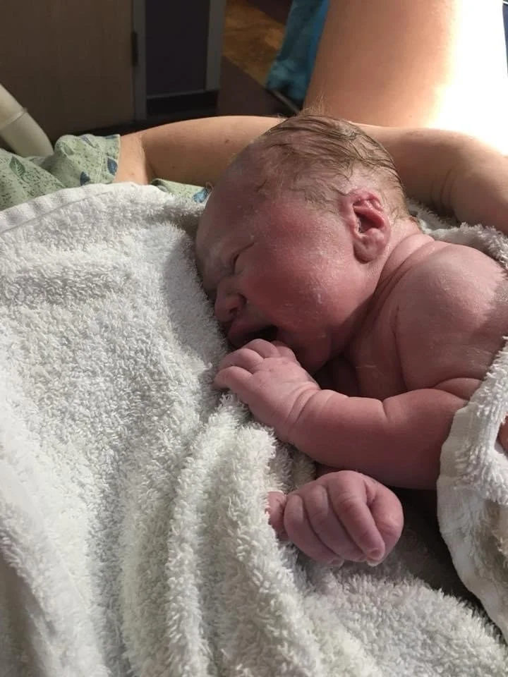 Newborn baby sleeping on a white towel, with a hand gently touching the baby's head.