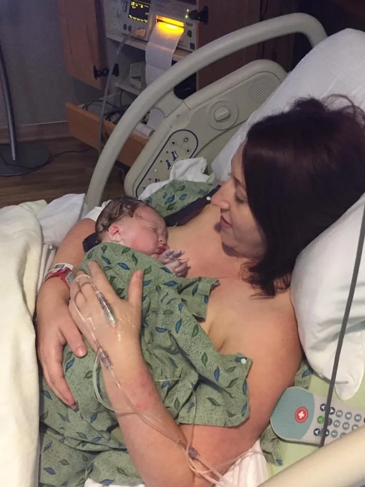 A mother lying in a hospital bed holding a newborn baby close to her chest, both resting peacefully.