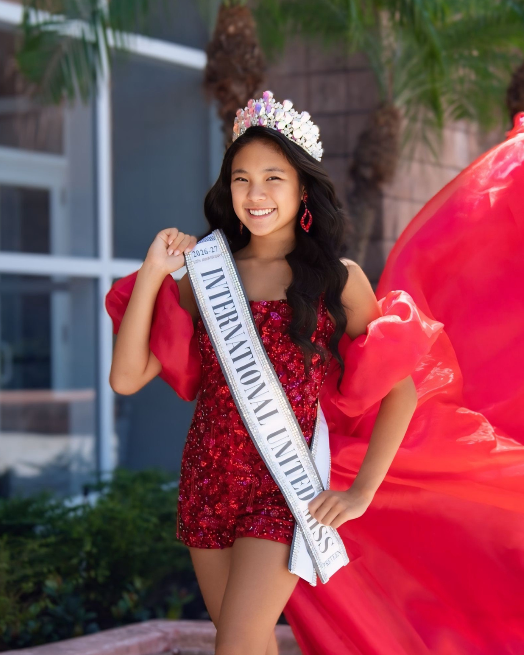 Young woman wearing a pink gown and tiara with a sash that reads 'International United Miss'.