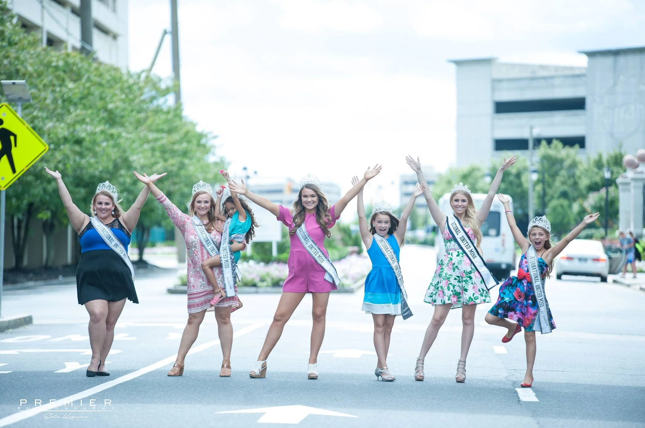 Group of young women wearing sashes and crowns, celebrating on a city street.