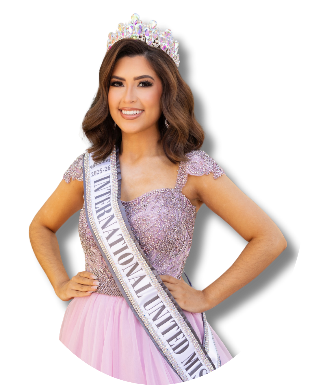 A young woman wearing a tiara, sash, and a pink gown with intricate beadwork, smiling confidently with one hand on her hip, against a black background.