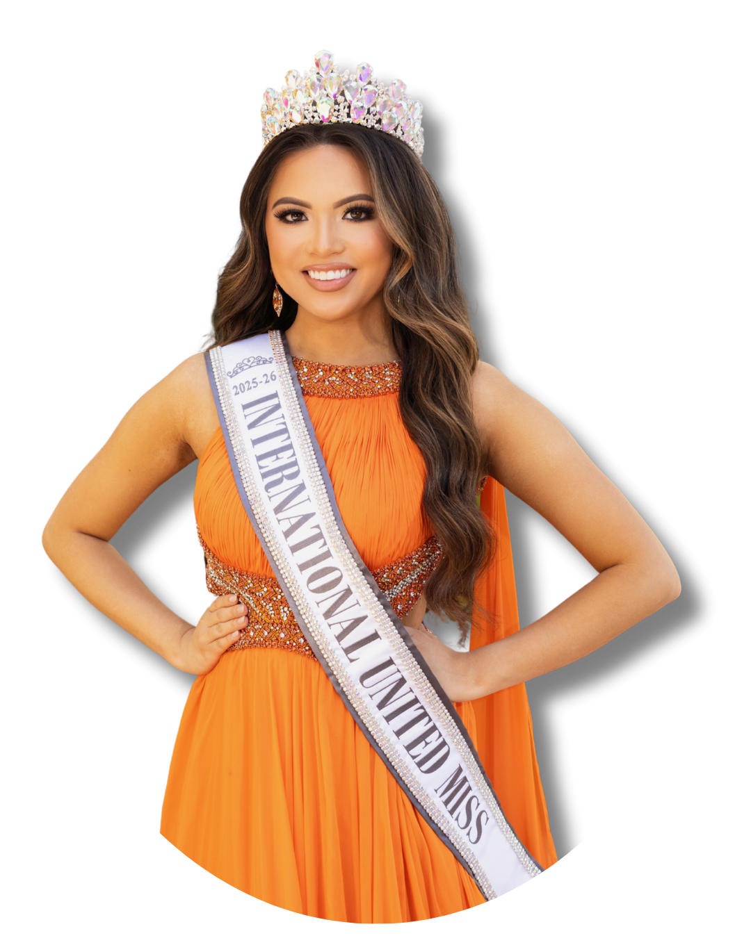 Miss International Woman wearing an orange gown, a crown, and a white sash that reads 'Miss International Woman 2025-26'. She is smiling and posing with hands on hips.