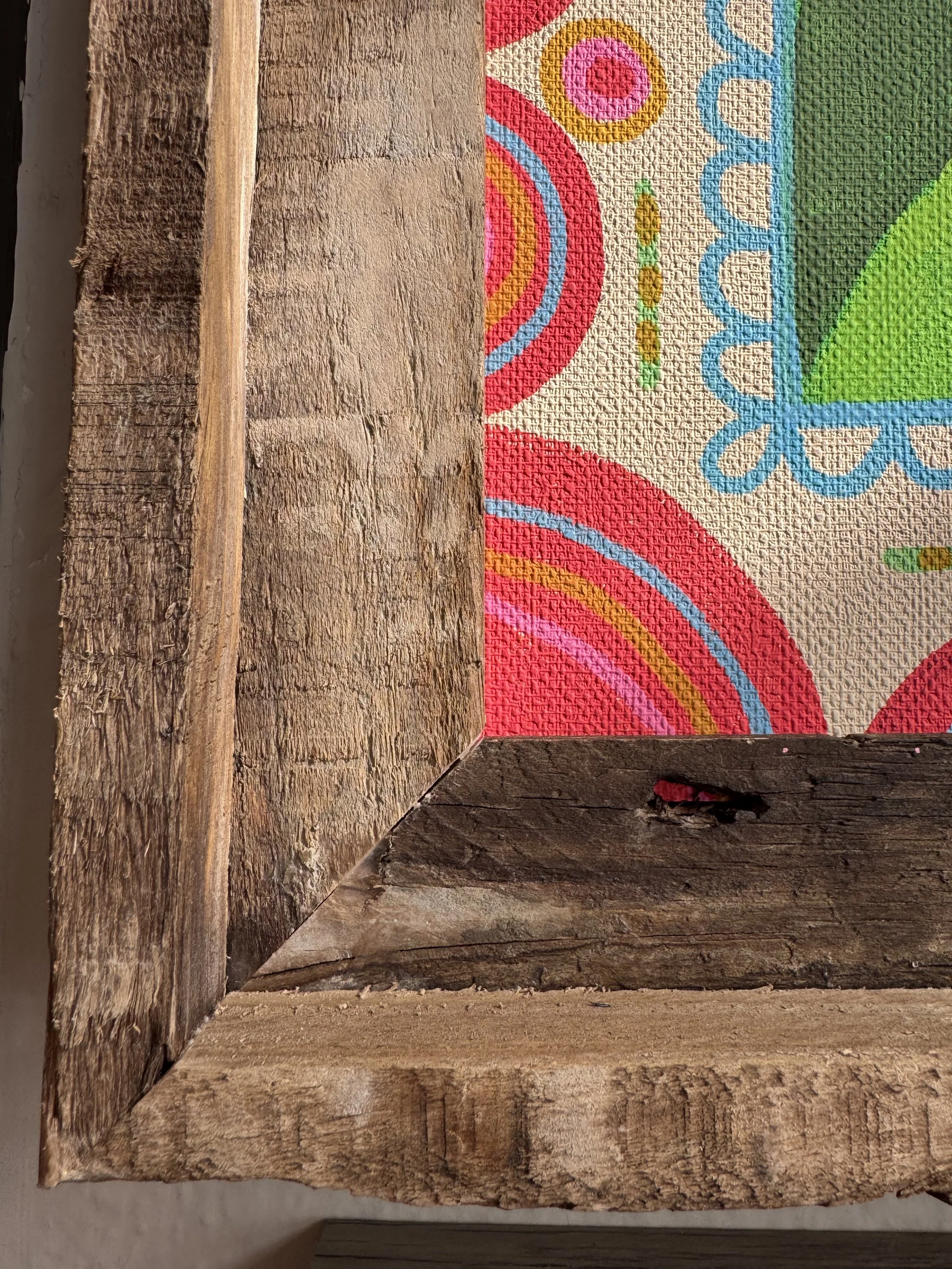Close-up of a wooden picture frame with a colorful, patterned textured background visible inside the frame.