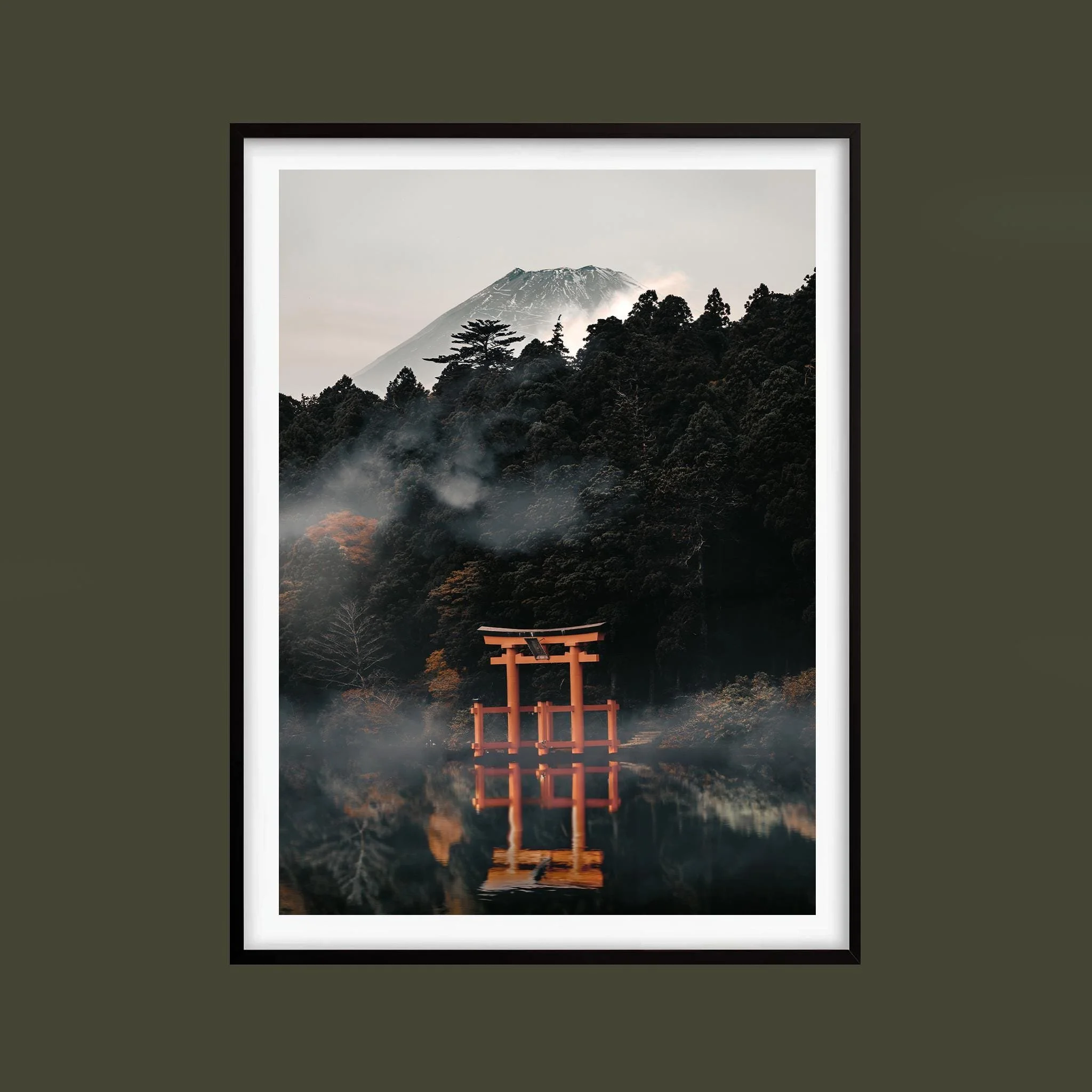 Red torii gate reflected in still water below misty forest and a mountain, shown in a black frame against an olive background. Frame not included.
