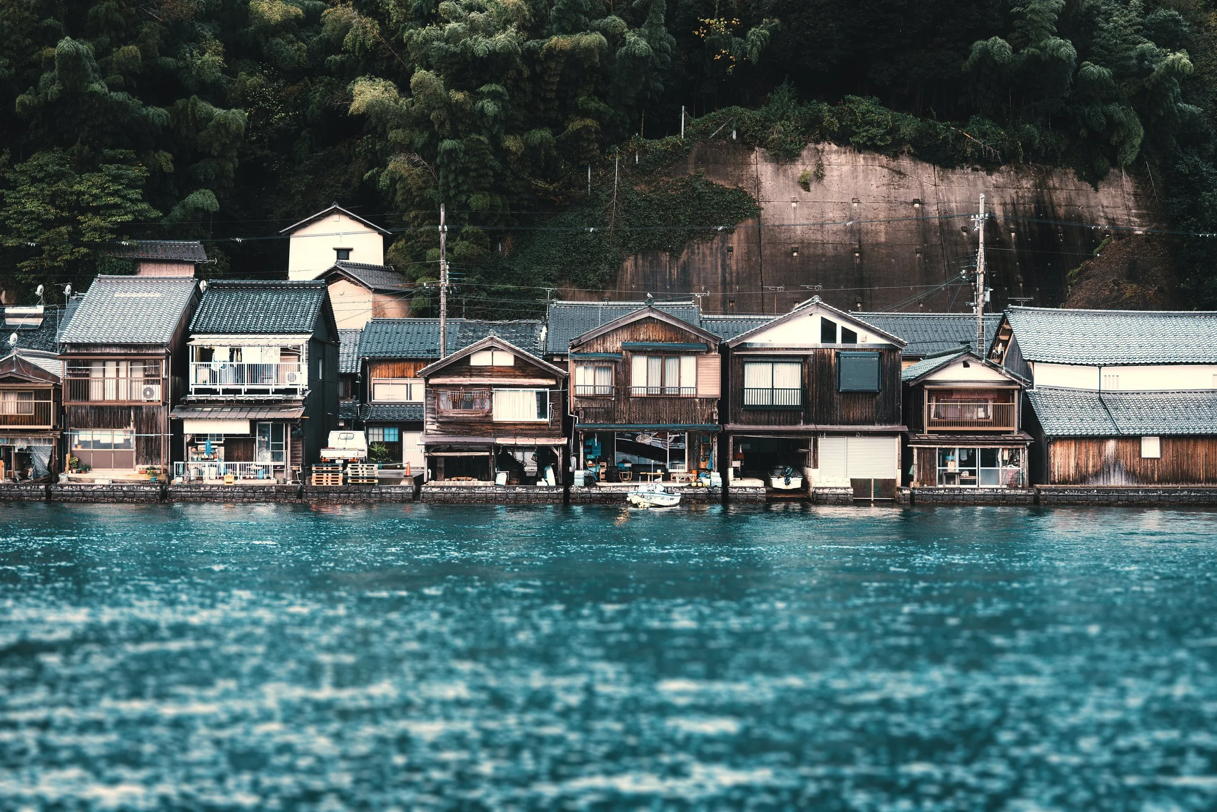 Timber boathouses beside blue water at Ine Bay, Japan. Personal travel photography by Latitude Frames.