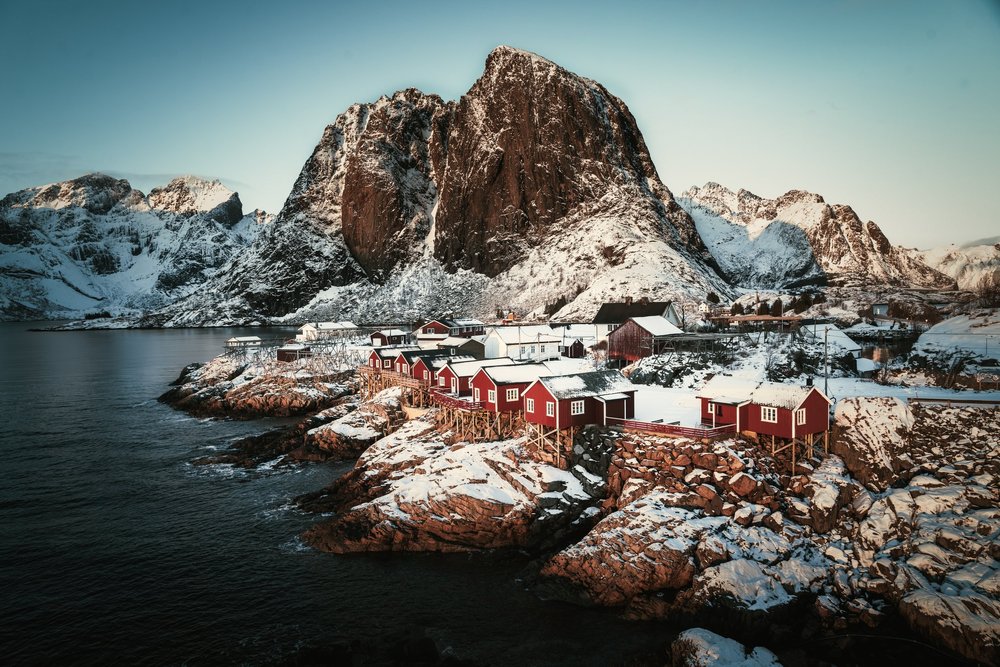 Hamnøy red cabins beside water and snowy mountains in Lofoten, Norway.