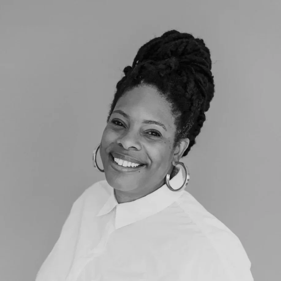 Professional headshot of an african american woman with a bun, earrings, a white shirt, against a light background