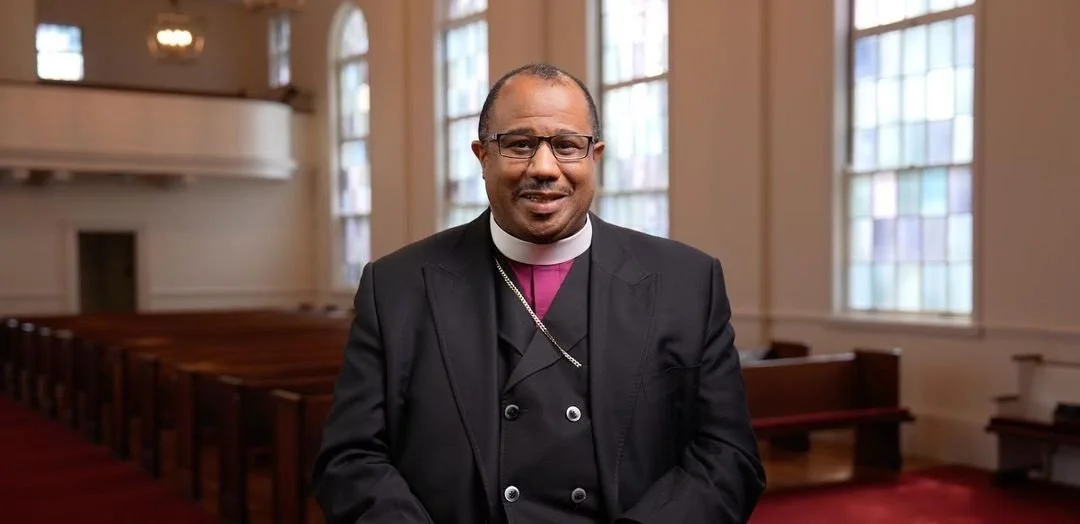 Professional headshot of a man in a dark suit, in a church setting.