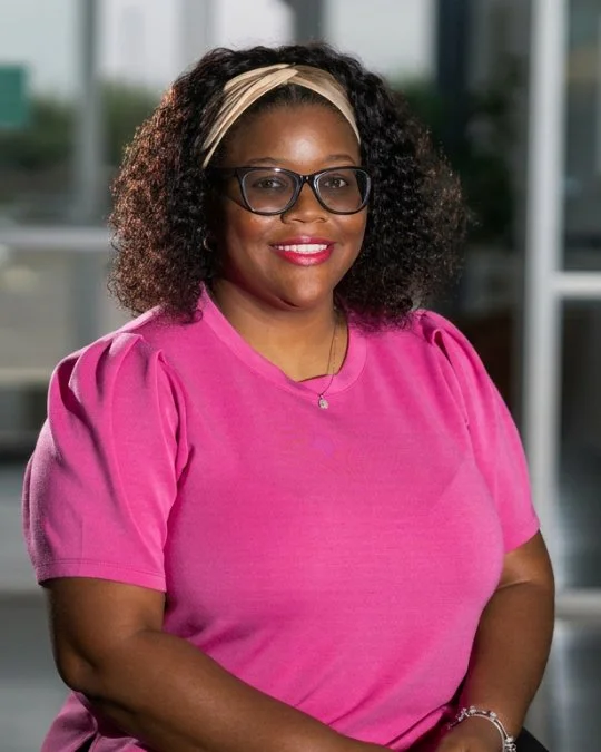 “Amber Bond, Kids Director, smiling in a studio portrait wearing a bright pink shirt.