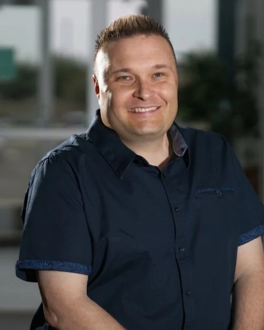 Pastor Jathan Gerdes, Lead Pastor, smiling in a studio portrait wearing a dark navy button-up shirt.