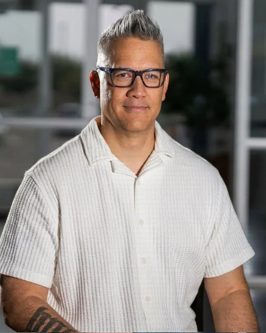 Pastor Sean Kelly, Creative Pastor, smiling in a studio portrait wearing a light textured button-up shirt.