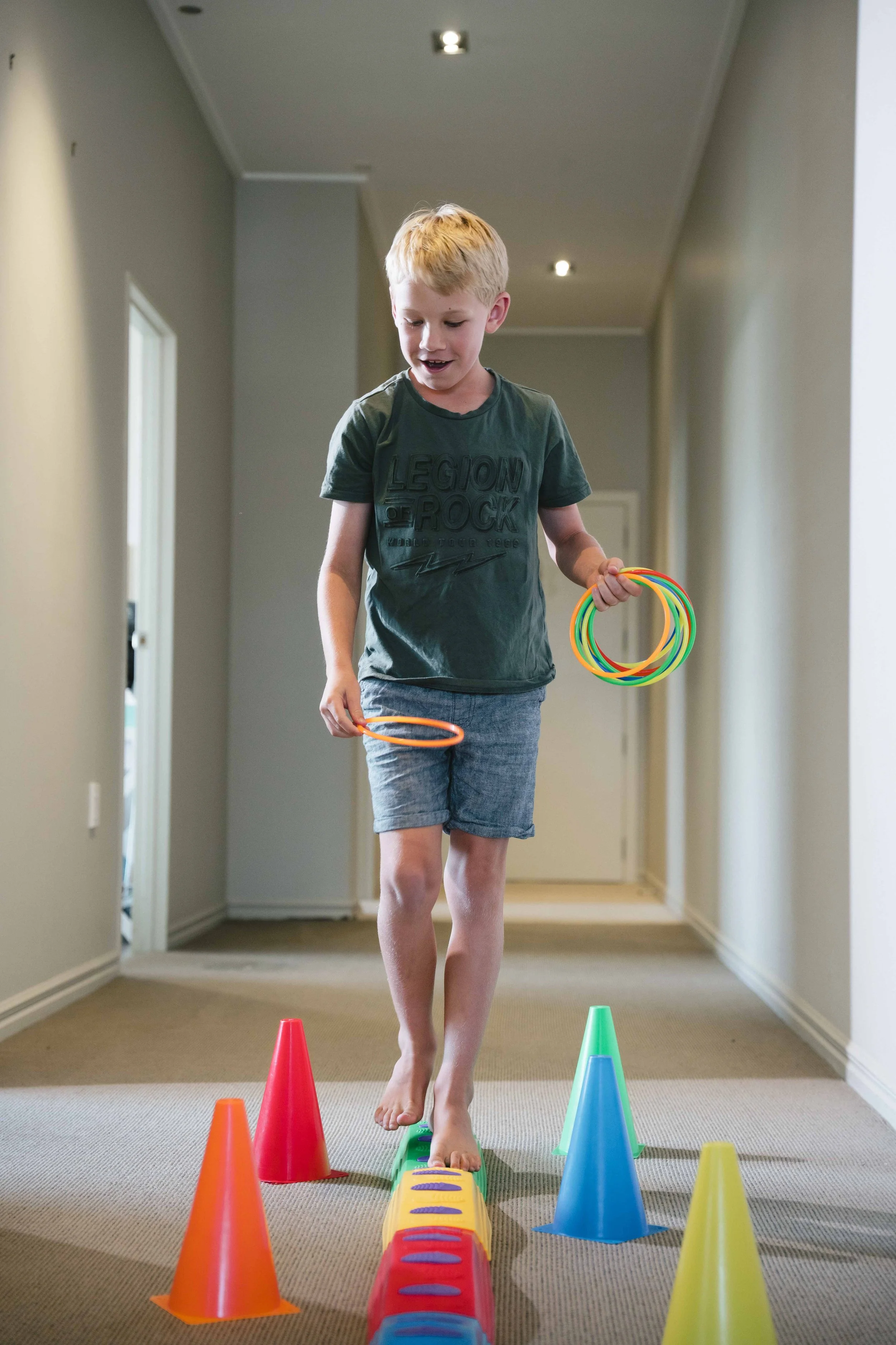 Child playing with colorful cones and rings indoors, walking barefoot on a narrow path.
