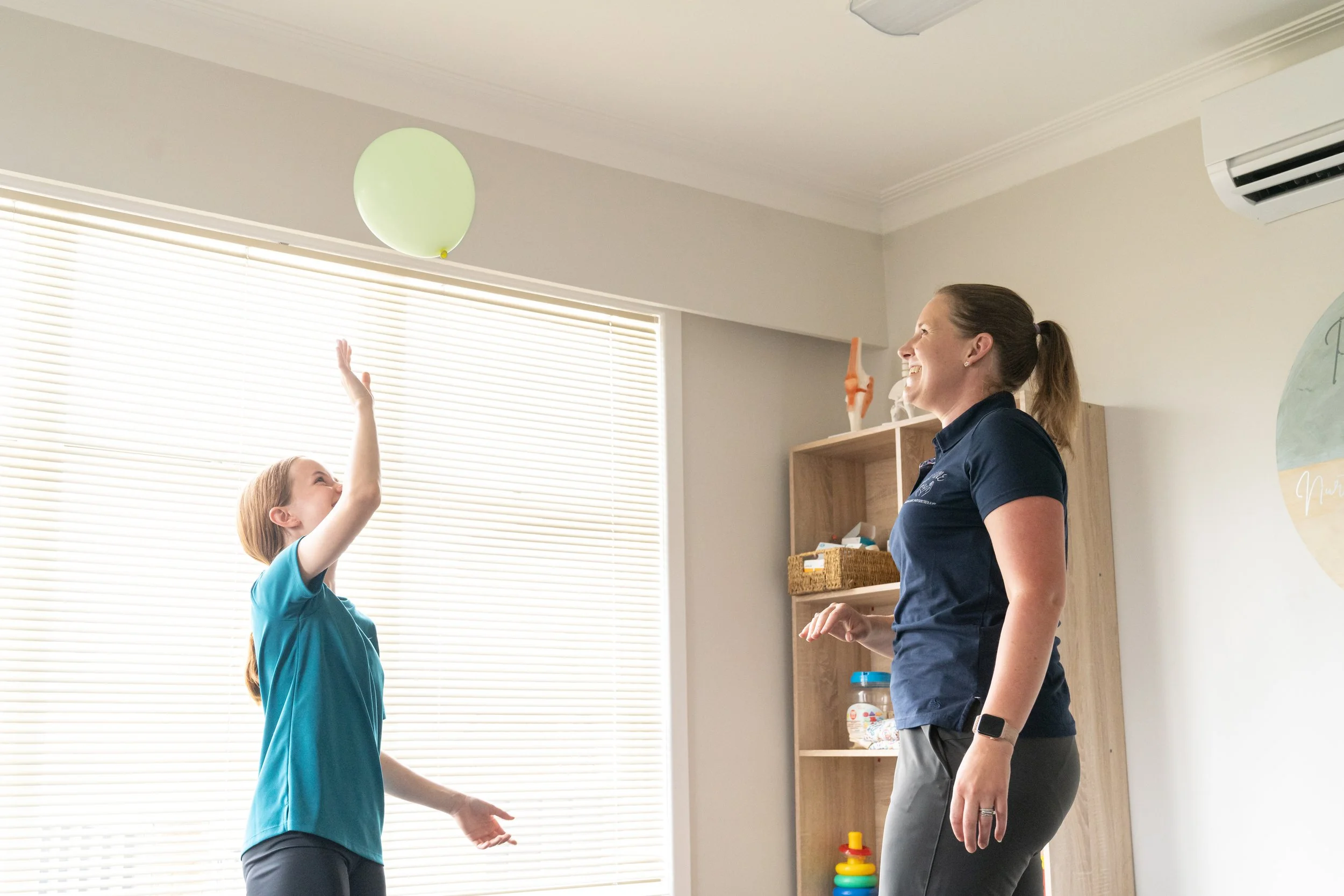Child and adult playing with a green balloon indoors.