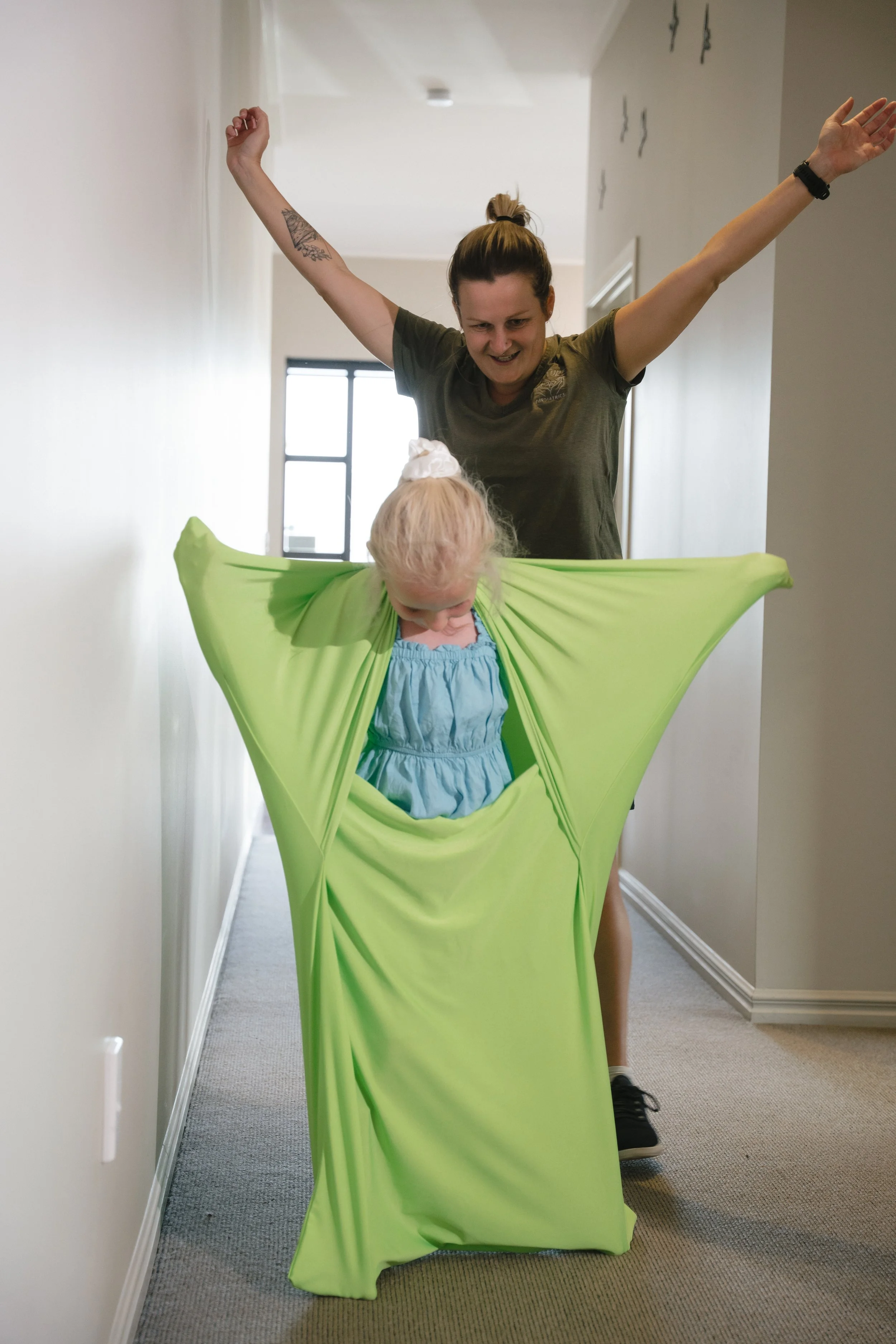 Child in green stretch fabric suit playing with adult behind in hallway.