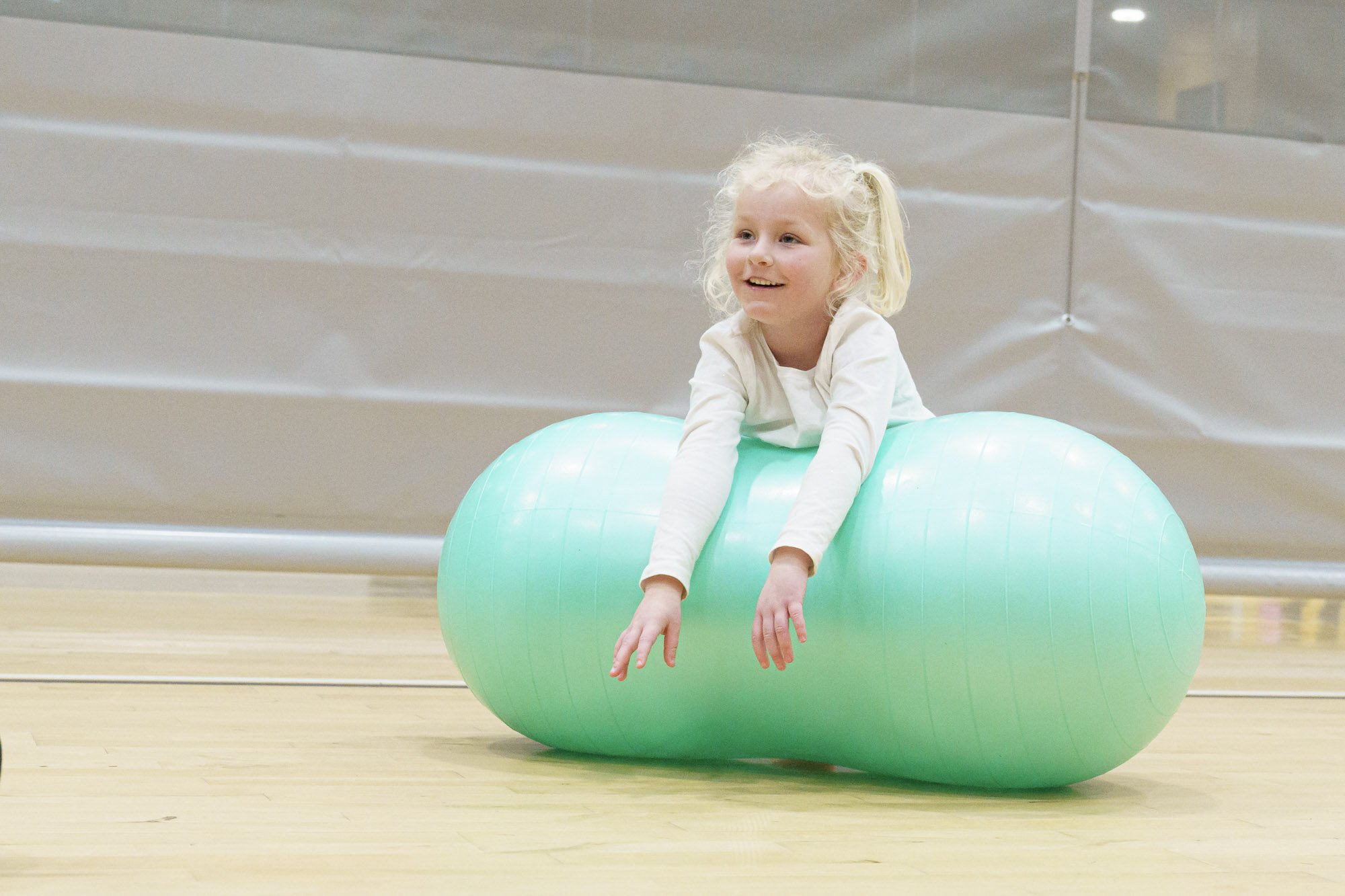 Child smiling while balancing on a light green peanut-shaped exercise ball indoors.
