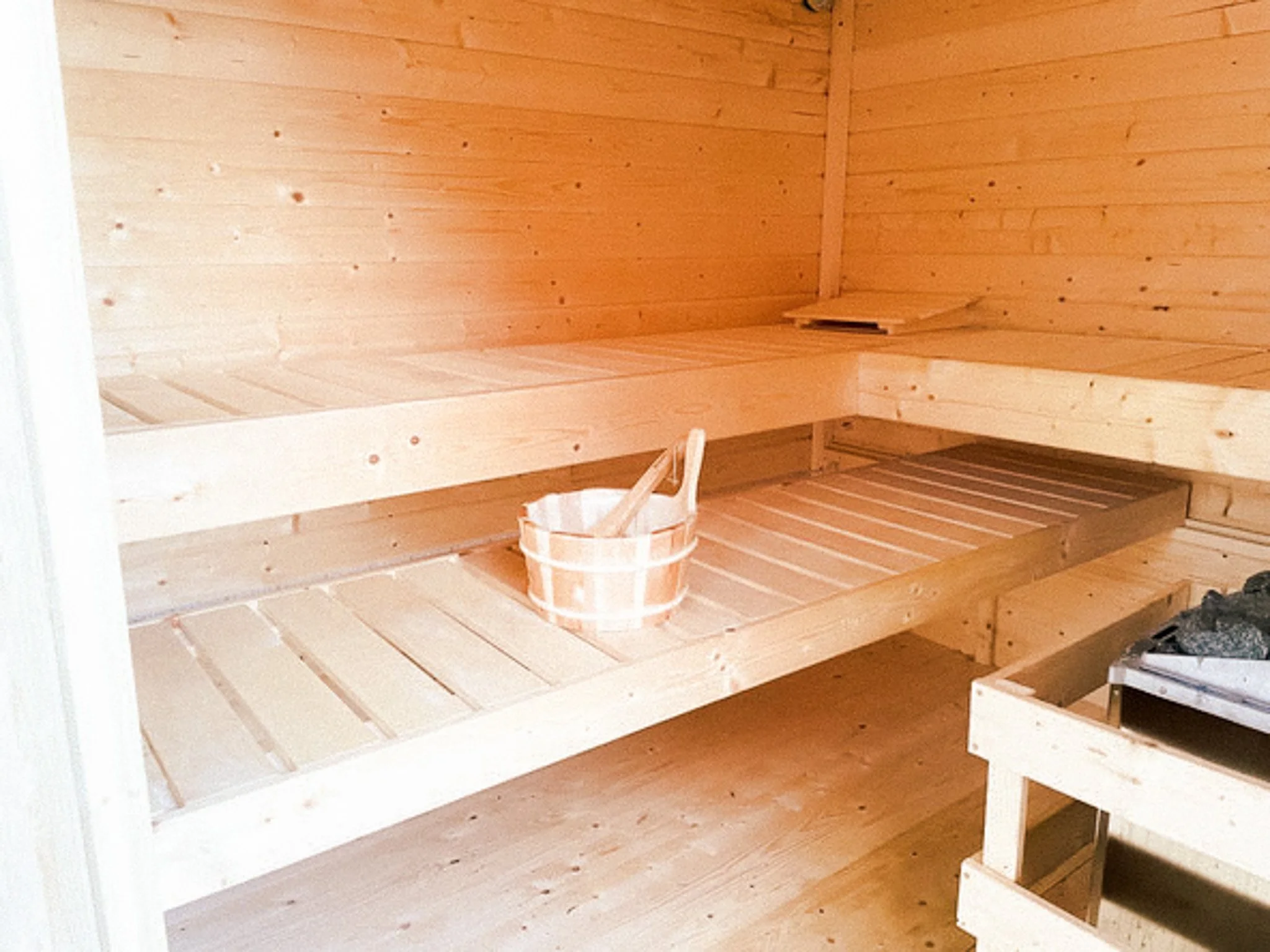 Innenansicht einer traditionellen Sauna mit Holzbänken und einem Holzkübel.