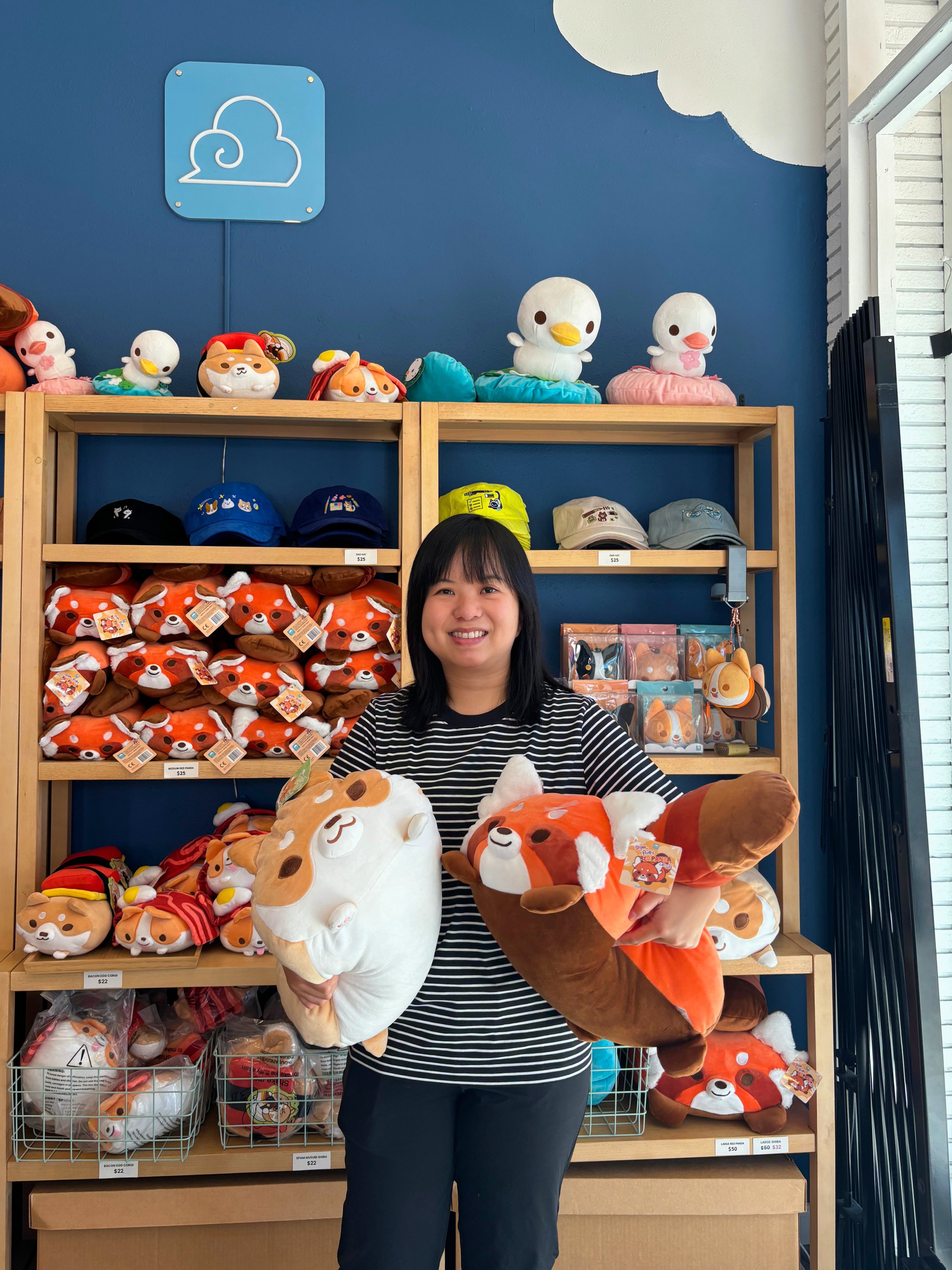 Elda The stands in front of her art creations and holds a corgi plushie at MOMENT Japantown
