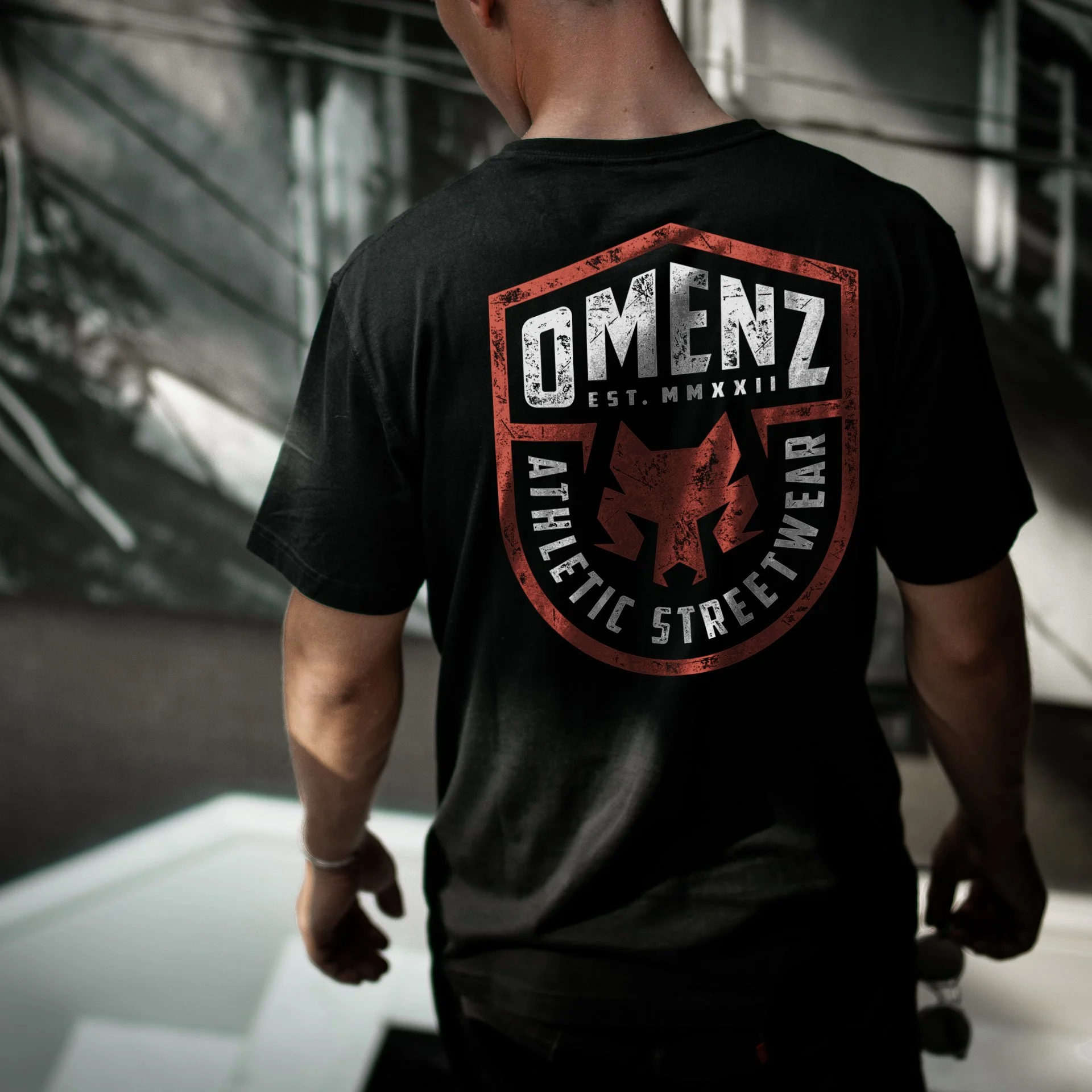 Back graphic on a black athletic streetwear shirt featuring the Omenz geometric wolf logo and badge design.